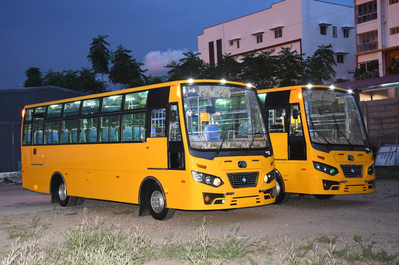 Two yellow Alfha institutional buses at dusk with interior lighting on, built in Karur